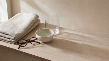 Balda de baño con toalla de lino, cuenco de agua y gafas: rutina de cuidado sencilla